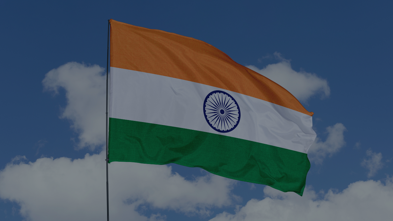 Flag of India flying against a blue sky with white clouds.